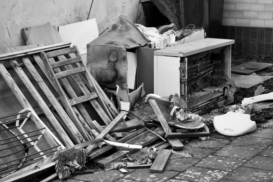 The image depicts a partially demolished brick building exterior, with sections of the wall torn away to reveal interior painted walls in white and light pink, surrounded by a large pile of rubble, br